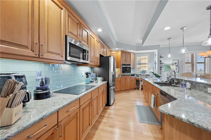 Kitchen with appliances with stainless steel finishes, ornamental molding, light wood finished floors, decorative backsplash, and light stone counters