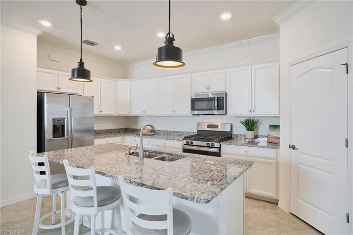 Kitchen large island featuring sink, hanging light fixtures, stainless steel appliances, an island with sink, and white cabinets