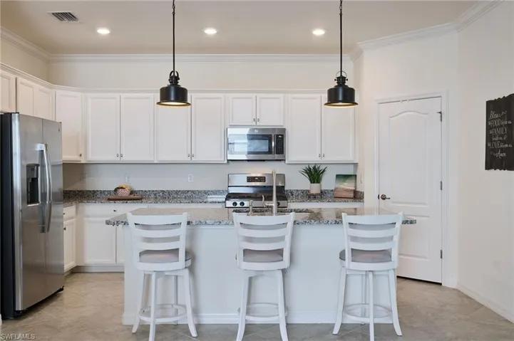Kitchen featuring stainless steel appliances, decorative light fixtures, a center island with sink, and white cabinets
