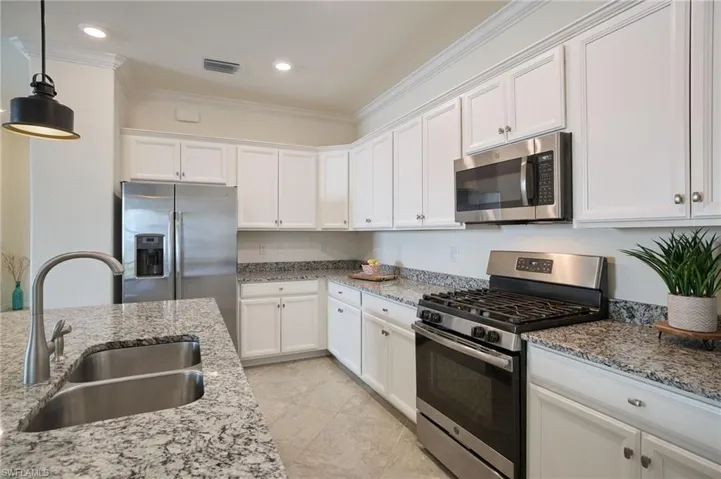 Kitchen with appliances with stainless steel finishes, pendant lighting, white cabinetry, sink, and light stone counters