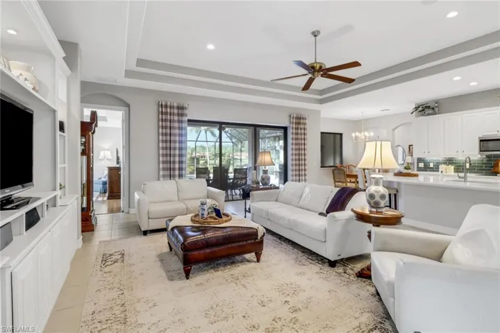 Living area with a raised ceiling, ceiling fan, recessed lighting, light tile patterned floors, and a chandelier