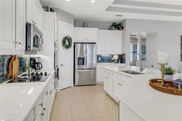 Kitchen with stainless steel appliances, decorative backsplash, light countertops, white cabinetry, and light tile patterned floors