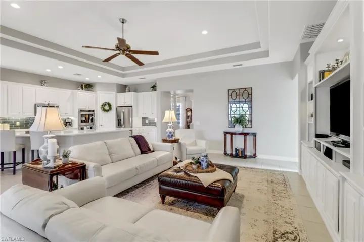 Living room with a tray ceiling, light tile patterned flooring, ceiling fan, and recessed lighting
