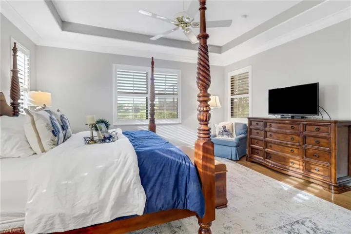 Bedroom with a tray ceiling, wood finished floors, ceiling fan, and crown molding