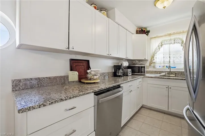Kitchen with white cabinets, appliances with stainless steel finishes, light stone counters, and light tile patterned flooring