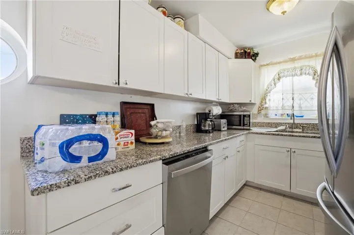 Kitchen with white cabinets, appliances with stainless steel finishes, light stone countertops, and light tile patterned floors