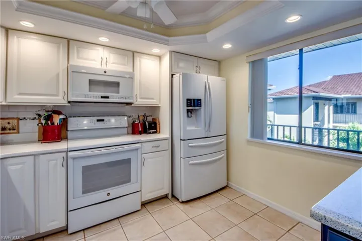 Kitchen featuring white cabinetry, white appliances, a raised ceiling, and decorative backsplash