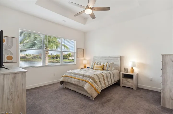 Carpeted bedroom featuring a raised ceiling and ceiling fan