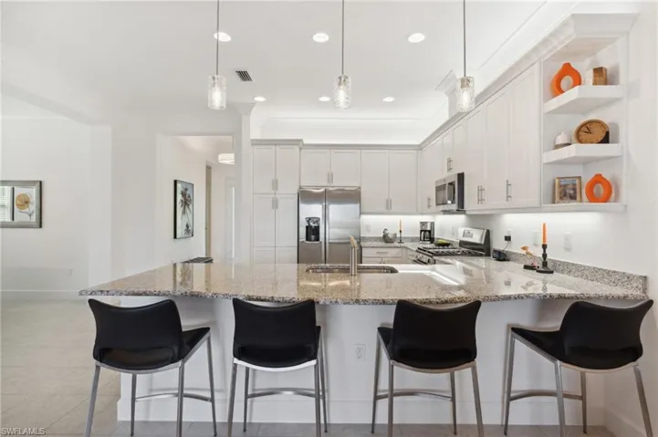 Kitchen featuring appliances with stainless steel finishes, a kitchen breakfast bar, sink, pendant lighting, and white cabinets