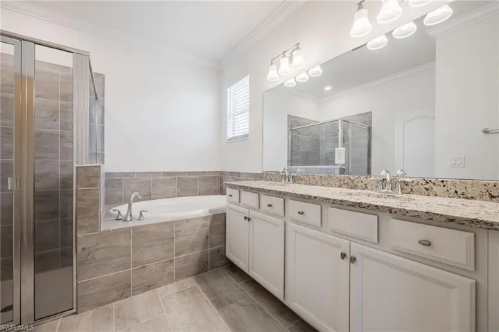 Full bath featuring a stall shower, a garden tub, double vanity, ornamental molding, and tile patterned floors