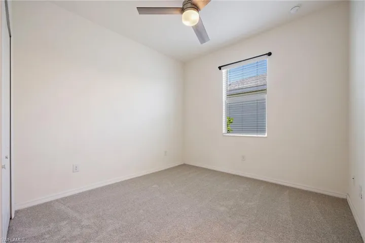 Carpeted spare room with a ceiling fan, baseboards, and a smoke detector