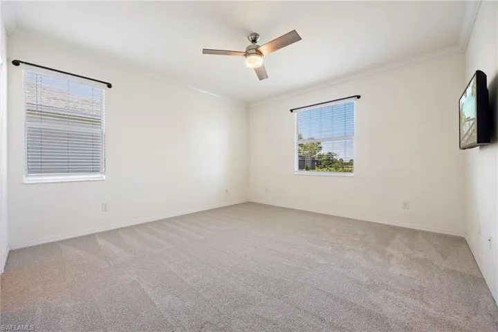 Empty room with carpet, a ceiling fan, crown molding, and baseboards