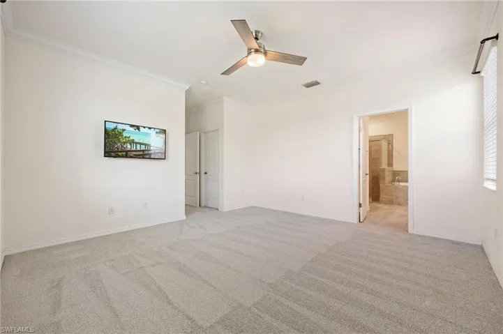Unfurnished bedroom featuring crown molding, light colored carpet, baseboards, a ceiling fan, and ensuite bath