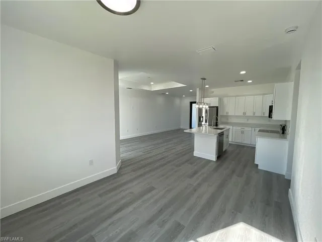 Kitchen with sink, a center island with sink, white cabinets, hardwood / wood-style floors, and hanging light fixtures
