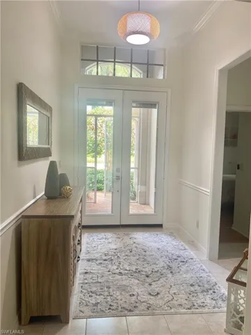 Foyer entrance with light tile patterned flooring, crown molding, french doors, and a healthy amount of sunlight