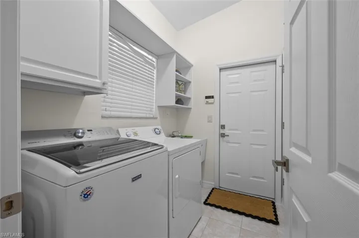 Clothes washing area featuring cabinets, light tile patterned flooring, and washing machine and dryer