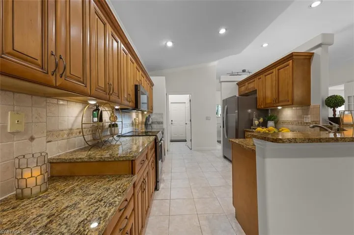 Kitchen featuring dark stone counters, light tile patterned floors, appliances with stainless steel finishes, kitchen peninsula, and backsplash