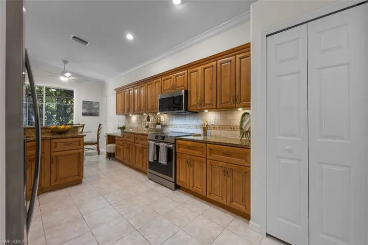 Kitchen with ornamental molding, appliances with stainless steel finishes, ceiling fan, and dark stone counters