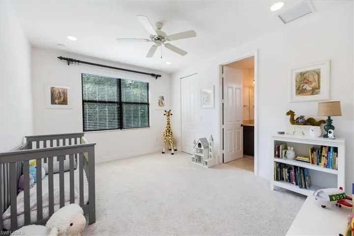 Bedroom featuring light carpet, ceiling fan, connected bathroom, a closet, and a crib