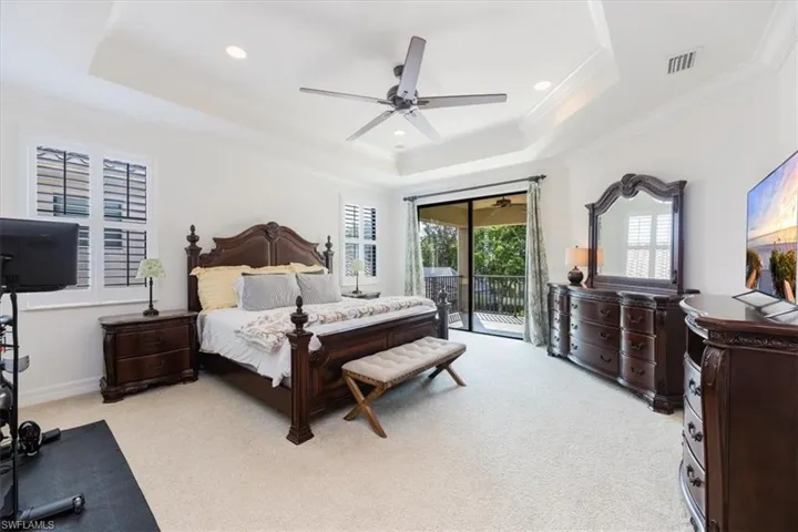 Bedroom featuring ceiling fan, light colored carpet, a raised ceiling, and access to exterior