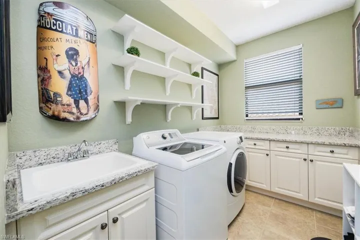 Laundry area featuring sink, light tile patterned floors, separate washer and dryer, and cabinets
