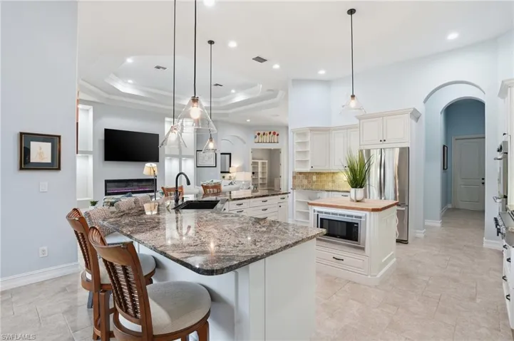 Kitchen with arched walkways, dark stone counters, open shelves, open floor plan, and decorative light fixtures