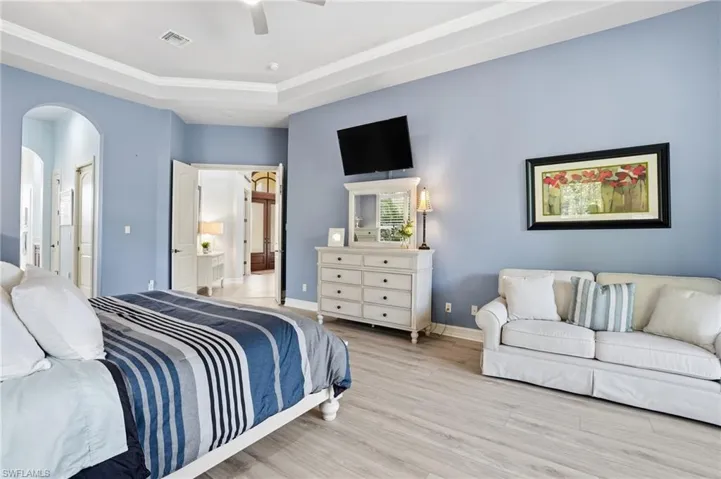 Bedroom featuring ensuite bathroom, wood finished floors, arched walkways, ceiling fan, and crown molding