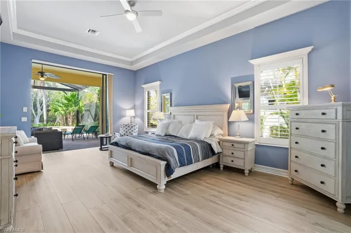 Bedroom with a tray ceiling, light wood-style floors, ceiling fan, and multiple windows