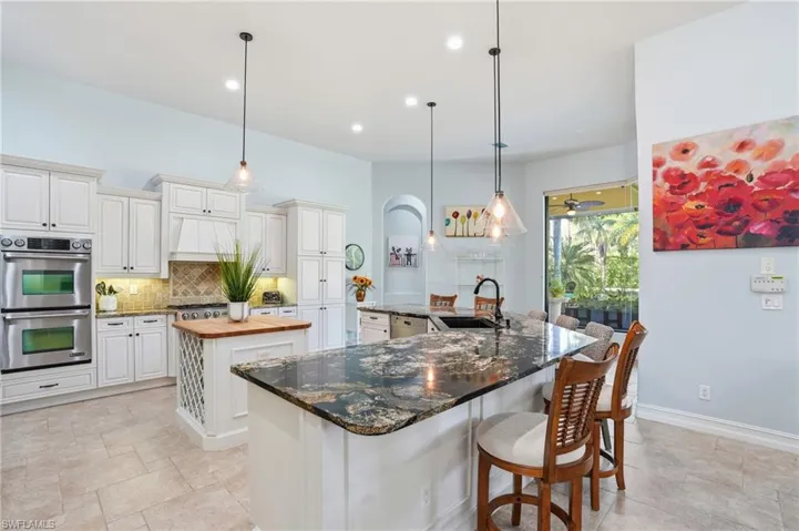 Kitchen with dark stone counters, stainless steel appliances, a breakfast bar area, decorative light fixtures, and tasteful backsplash