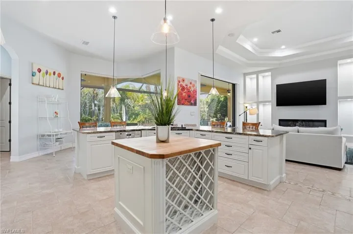 Kitchen featuring white cabinets, open floor plan, decorative light fixtures, dark stone countertops, and a raised ceiling