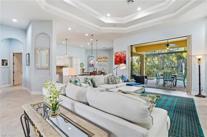 Living room featuring ornamental molding, arched walkways, a sunroom, recessed lighting, and a raised ceiling