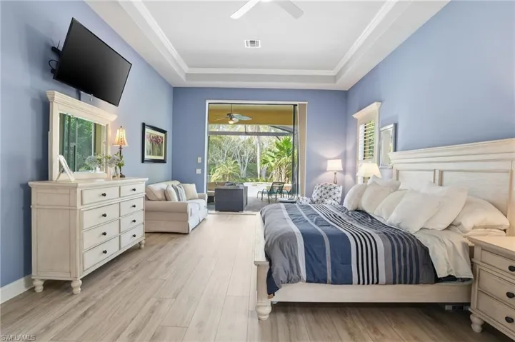 Bedroom with access to outside, light wood-style flooring, a tray ceiling, and a ceiling fan
