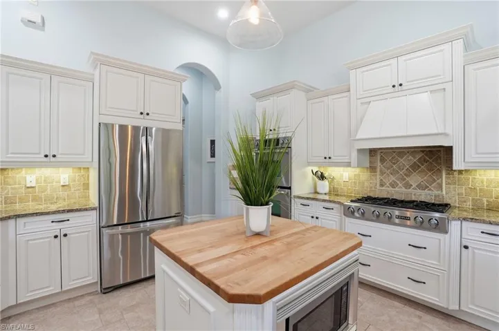 Kitchen featuring tasteful backsplash, appliances with stainless steel finishes, light stone counters, premium range hood, and arched walkways