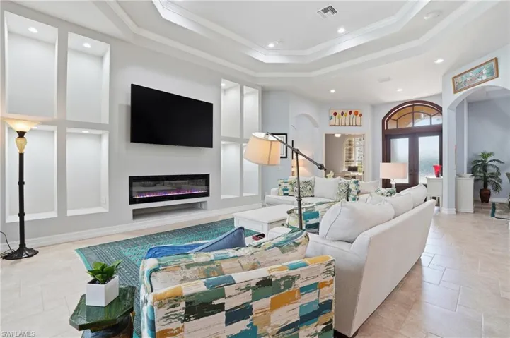 Living area featuring a glass covered fireplace, ornamental molding, recessed lighting, a raised ceiling, and arched walkways