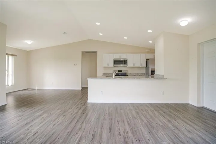Open Kitchen with vaulted ceiling, elegant granite countertops,  stainless steel appliances and white sleek cabinets.