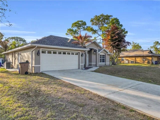 Ranch-style house featuring stucco siding, concrete driveway, a shingled roof, and a front yard