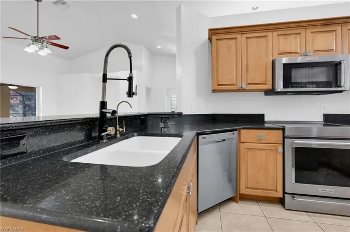Kitchen featuring stainless steel appliances, dark stone countertops, lofted ceiling, a ceiling fan, and light tile patterned floors