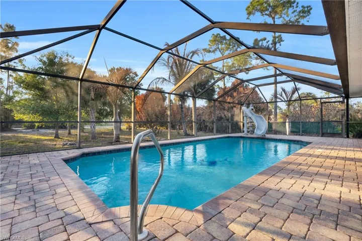 Swimming pool featuring glass enclosure, a sunroom, a water slide, and a patio