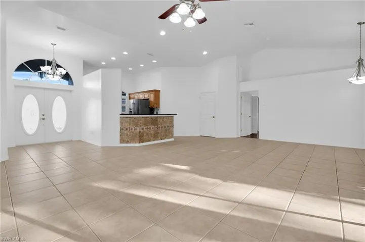 Unfurnished living room with suspended lighting, ceiling fan, light tile patterned flooring, and vaulted ceiling