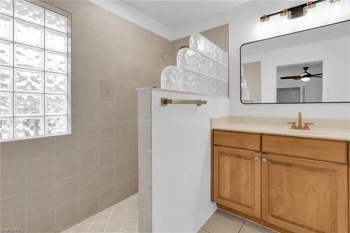 Full bathroom featuring a walk in shower, vanity, light tile patterned flooring, and ceiling fan