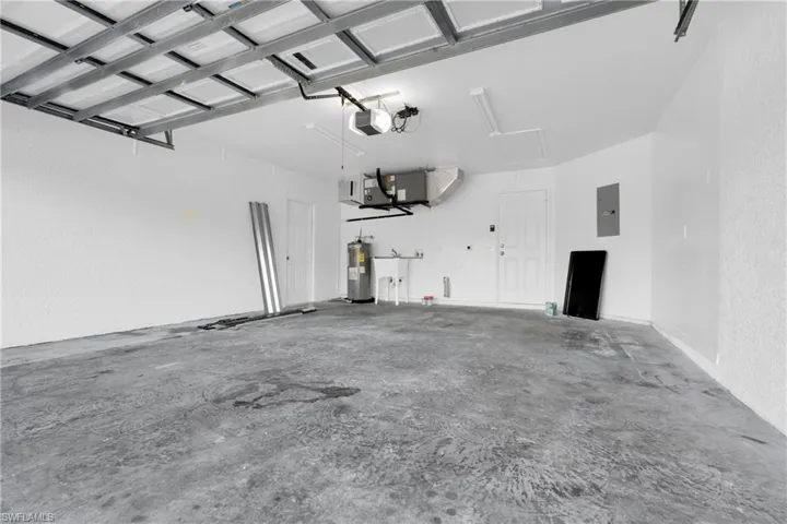 Garage with electric panel, electric water heater, heating unit, and a garage door opener