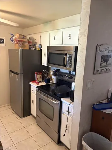 Kitchen featuring white cabinetry, stainless steel refrigerator, stainless steel electric range, and over-the-range microwave with tile flooring