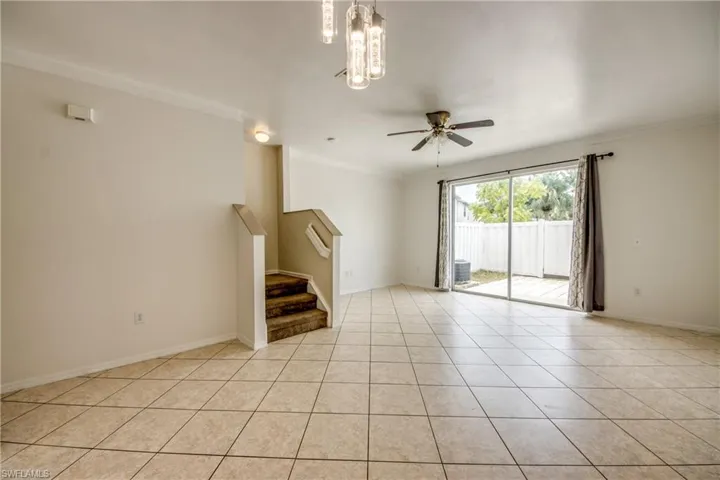 Spare room with ornamental molding, light tile floors, and ceiling fan with notable chandelier