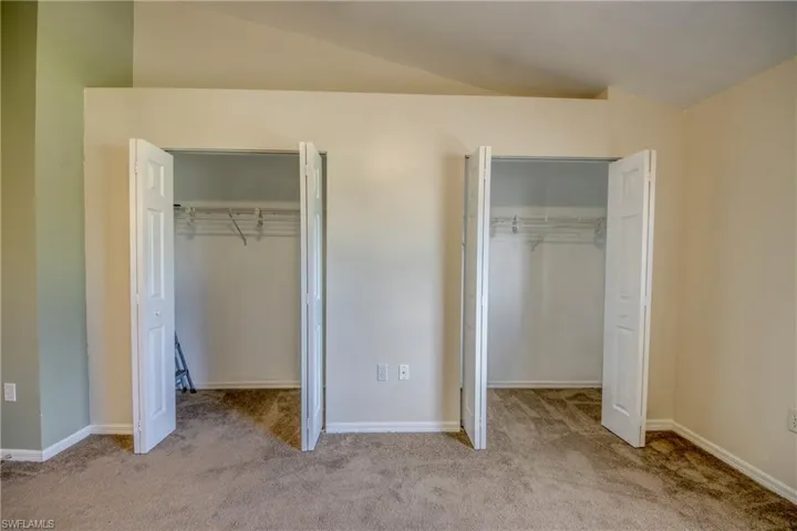 Unfurnished bedroom featuring vaulted ceiling, light carpet, and multiple closets