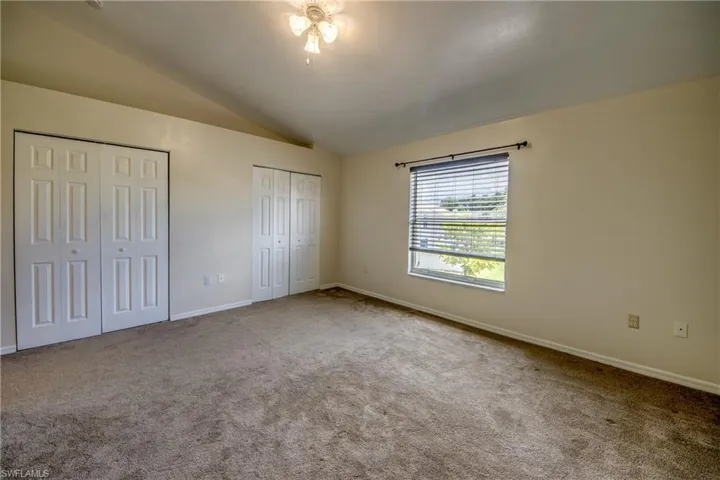 Unfurnished bedroom with two closets, carpet flooring, and vaulted ceiling
