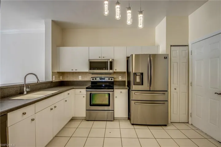 Kitchen featuring light tile flooring, pendant lighting, sink, white cabinetry, and appliances with stainless steel finishes