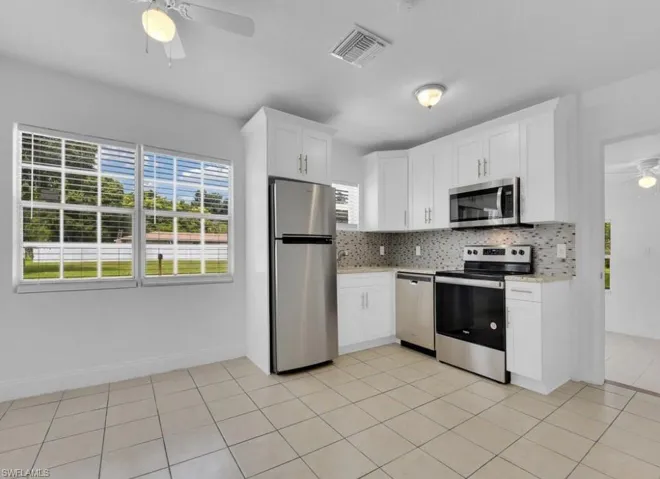 Kitchen with ceiling fan, appliances with stainless steel finishes, white cabinetry, light tile patterned floors, and backsplash