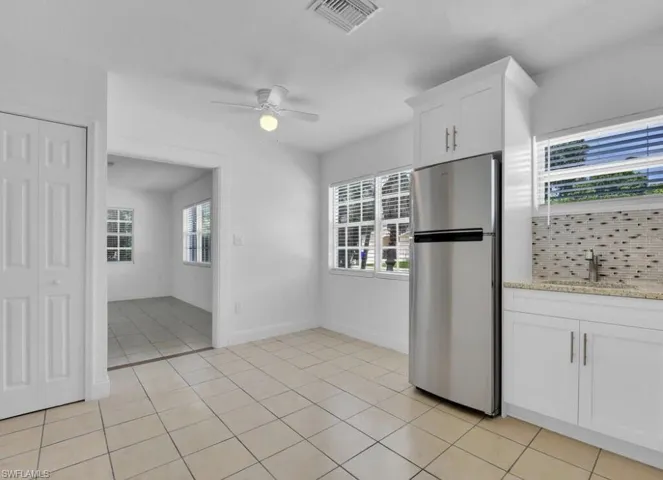 Kitchen with freestanding refrigerator, white cabinetry, light stone countertops, light tile patterned flooring, and ceiling fan