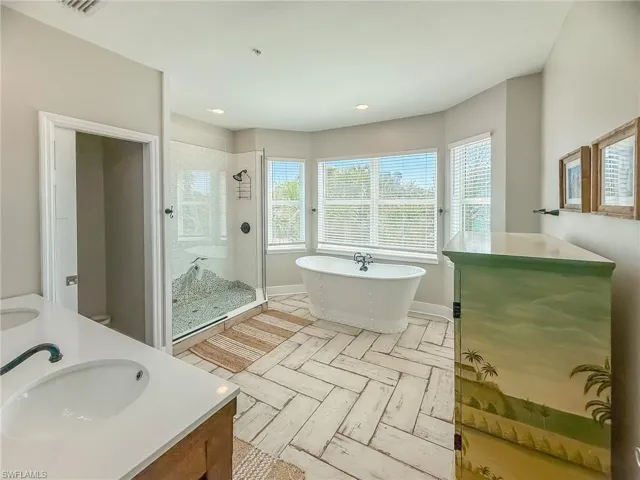Full bathroom featuring baseboards, double vanity, a stall shower, a soaking tub, and a sink