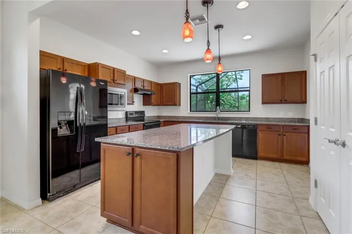 Kitchen featuring black appliances, under cabinet range hood, brown cabinets, hanging light fixtures, and recessed lighting